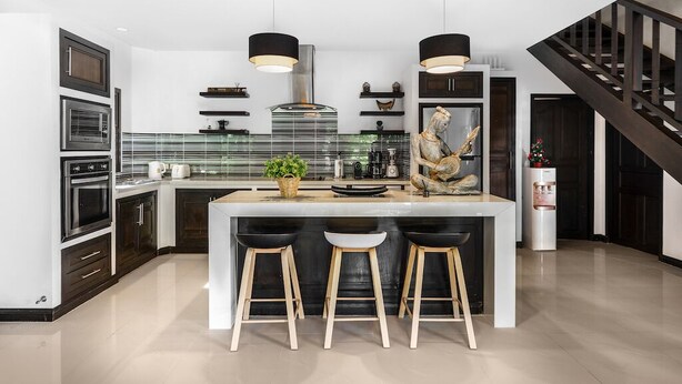 Una cocina moderna con una isla central, taburetes de bar, iluminación colgante y una escalera.