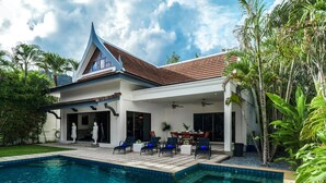 Una casa moderna con piscina, mobiliario de exterior y vegetación tropical.