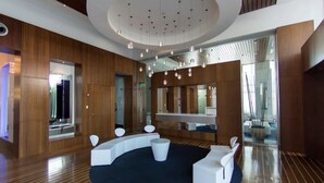 Eine moderne, gut beleuchtete Lobby mit Holzvertäfelung, einer runden Sitzecke und einem großen Spiegel, der den Raum widerspiegelt.