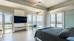 Ein modernes Schlafzimmer mit einem großen Bett, einem an der Wand montierten Fernseher und großen Fenstern mit Blick auf die Stadt.