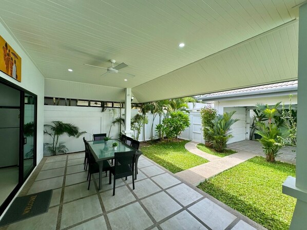 A modern patio with a glass table and chairs, surrounded by a well-maintained lawn and potted plants.