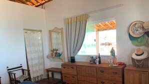 Une chambre à coucher avec un lit, une commode en bois, un banc, un miroir et une fenêtre avec des rideaux.