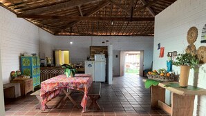 Une cuisine spacieuse avec un sol carrelé, un plafond en bois et un coin repas doté d’une table recouverte d’une nappe colorée.