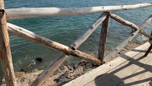 Une jetée en bois s’étendant sur une étendue d’eau calme, avec une plage de sable en arrière-plan.