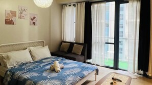 Une chambre à coucher comprenant un lit, une table de chevet, un canapé, une fenêtre avec des rideaux et un luminaire au plafond.