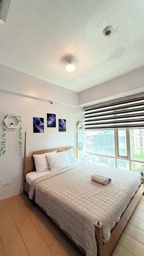 A bedroom with a bed, a window with blinds, a ceiling light, and wall decorations. - Henry's Newport (Pasay)