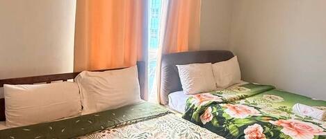Un dormitorio con dos camas, una ventana con cortinas y una puerta a la vista.