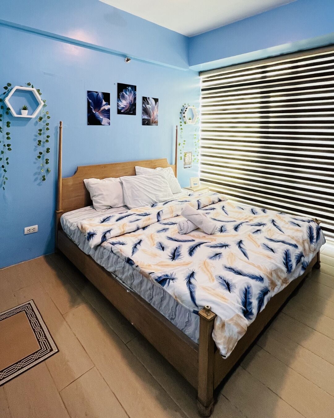 Une chambre à coucher avec un lit, des murs bleus et une fenêtre avec des stores.
