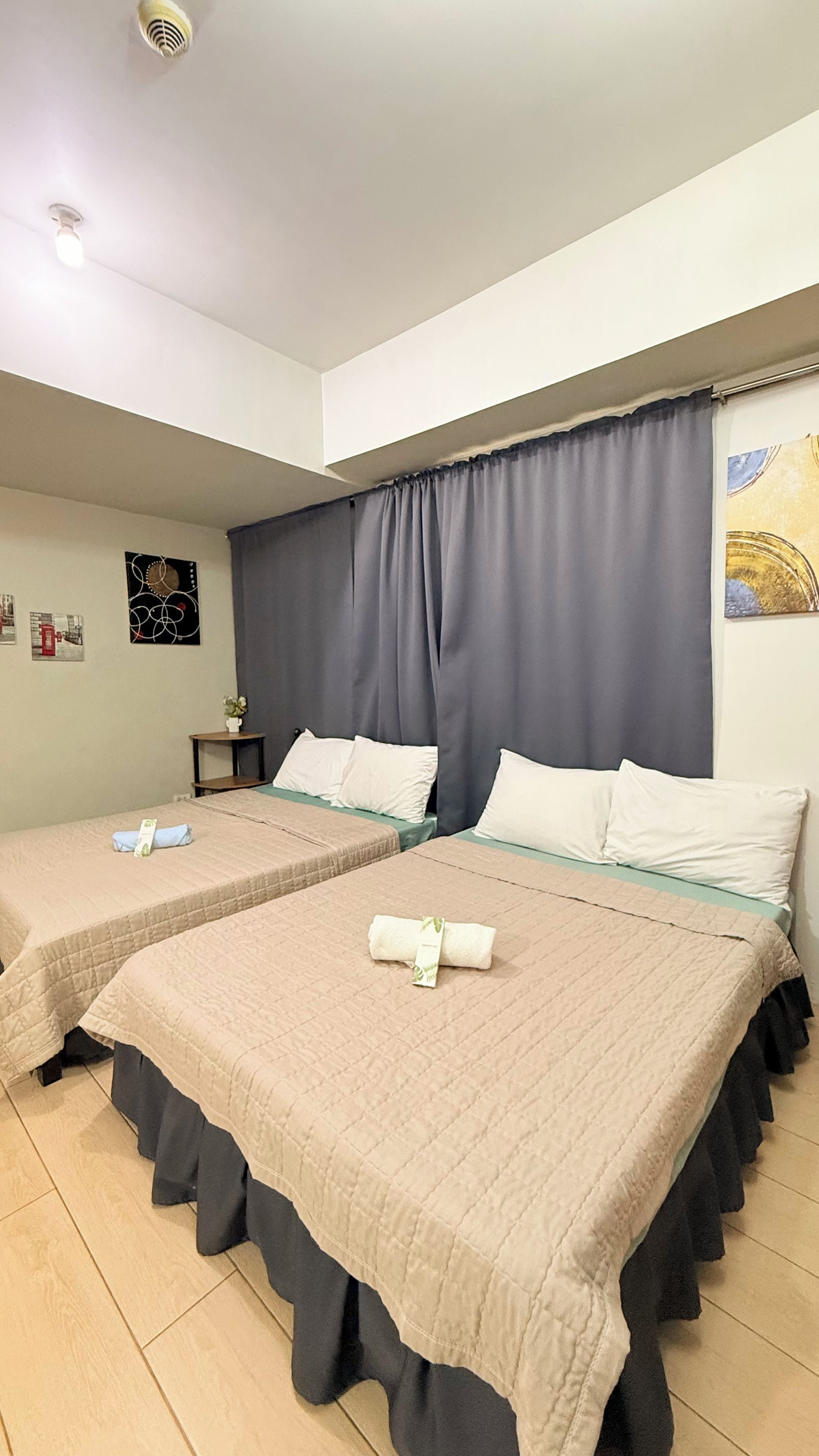 A hotel room with two beds, a small table, and a wall with artwork.