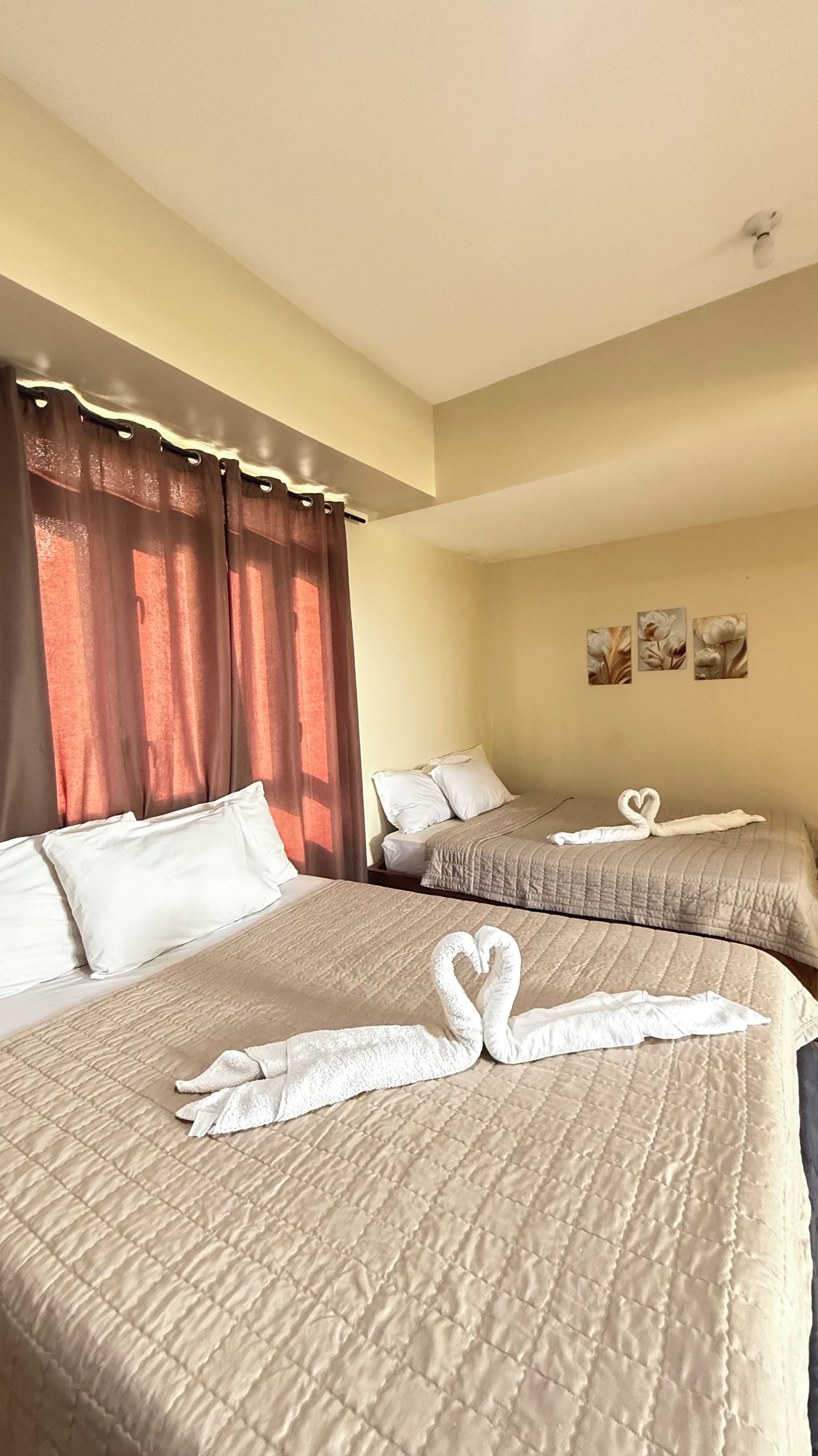A hotel room with two beds, each with a quilted bedspread and pillows. There are decorative swan-shaped towels on the beds.