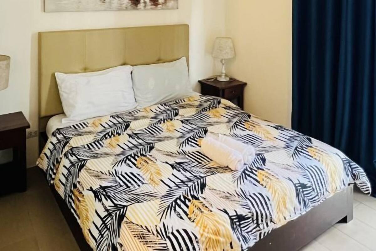 Una cama con una colcha de estampado de hojas, una lámpara de noche y una mesita de noche.