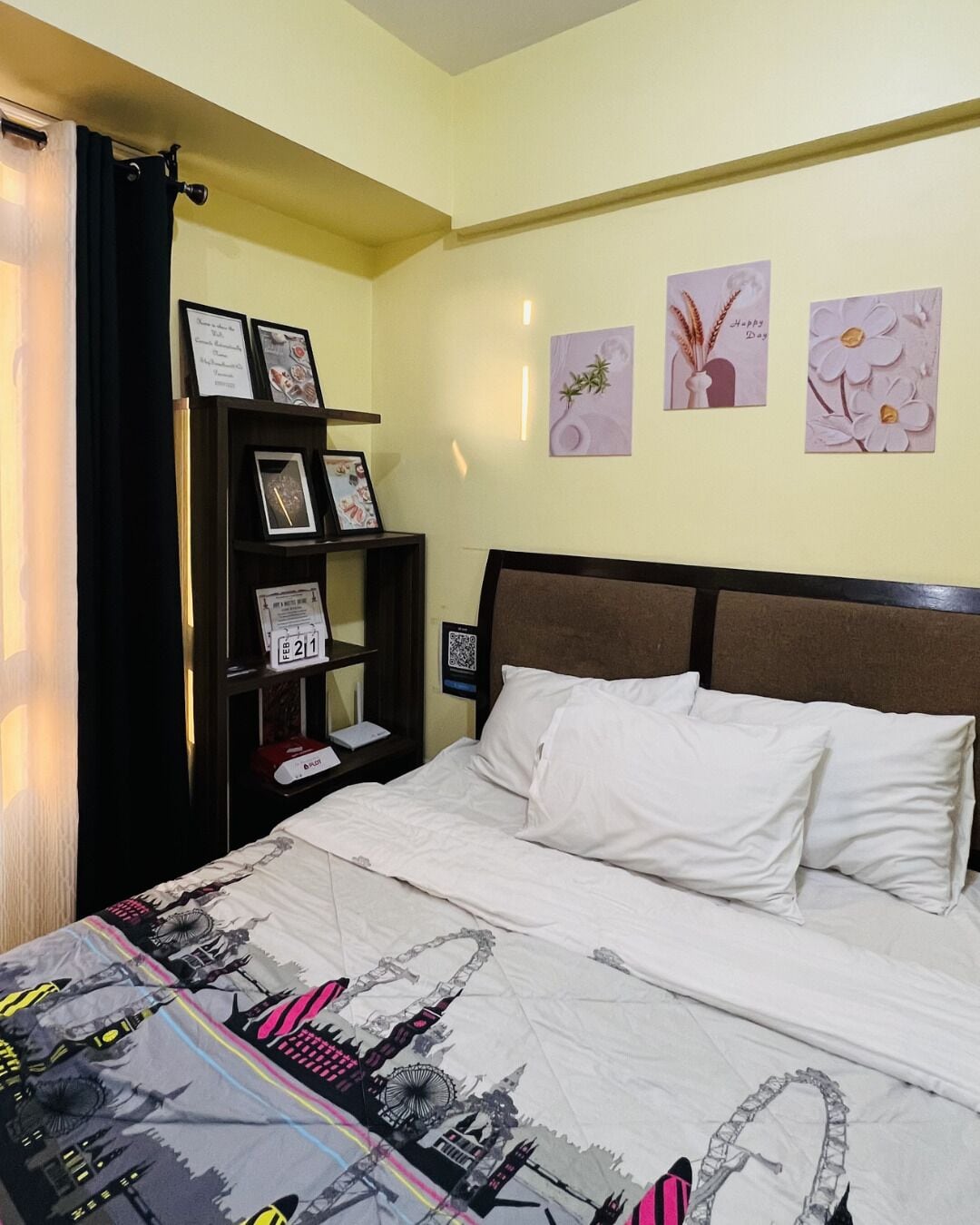 Un dormitorio con cama, mesita de noche, estante con fotos enmarcadas y decoración en la pared.