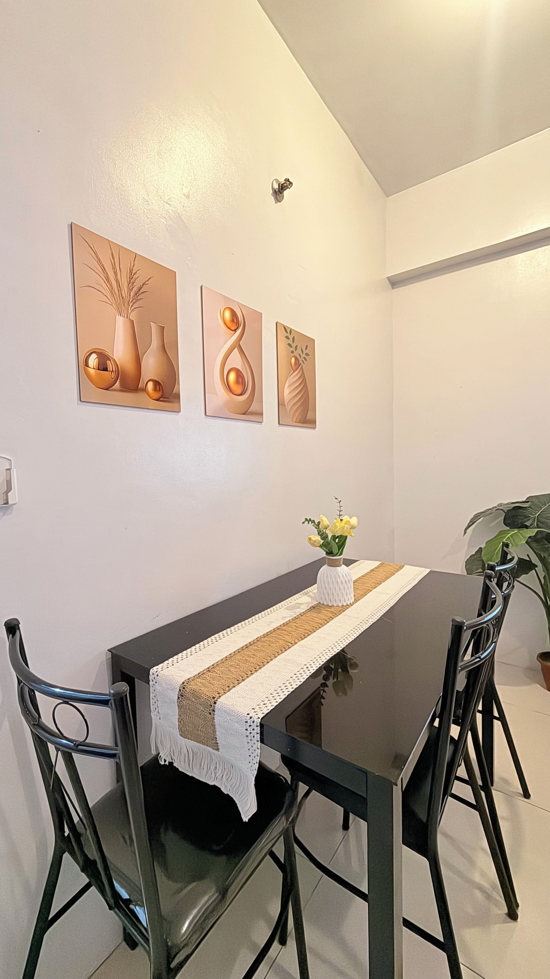Un coin repas avec une table noire, une nappe blanche et quatre chaises. Trois œuvres d’art encadrées sont accrochées au-dessus de la table.