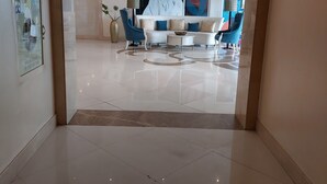 Un hall d’entrée moderne avec un sol carrelé de blanc, un canapé bleu, une table basse blanche et un grand tableau abstrait accroché au mur.