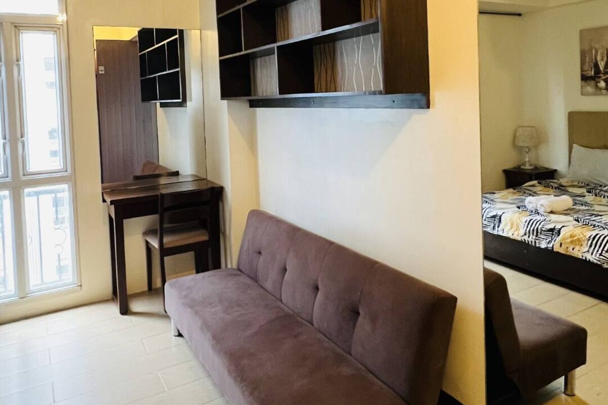 Habitación con sofá, escritorio, estantería y cama con colcha estampada.