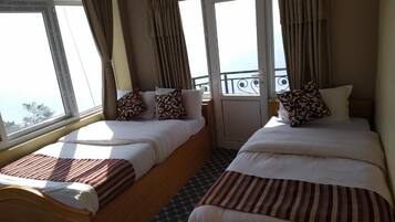 Two single beds with striped blankets, a window with curtains, and a balcony with a railing.