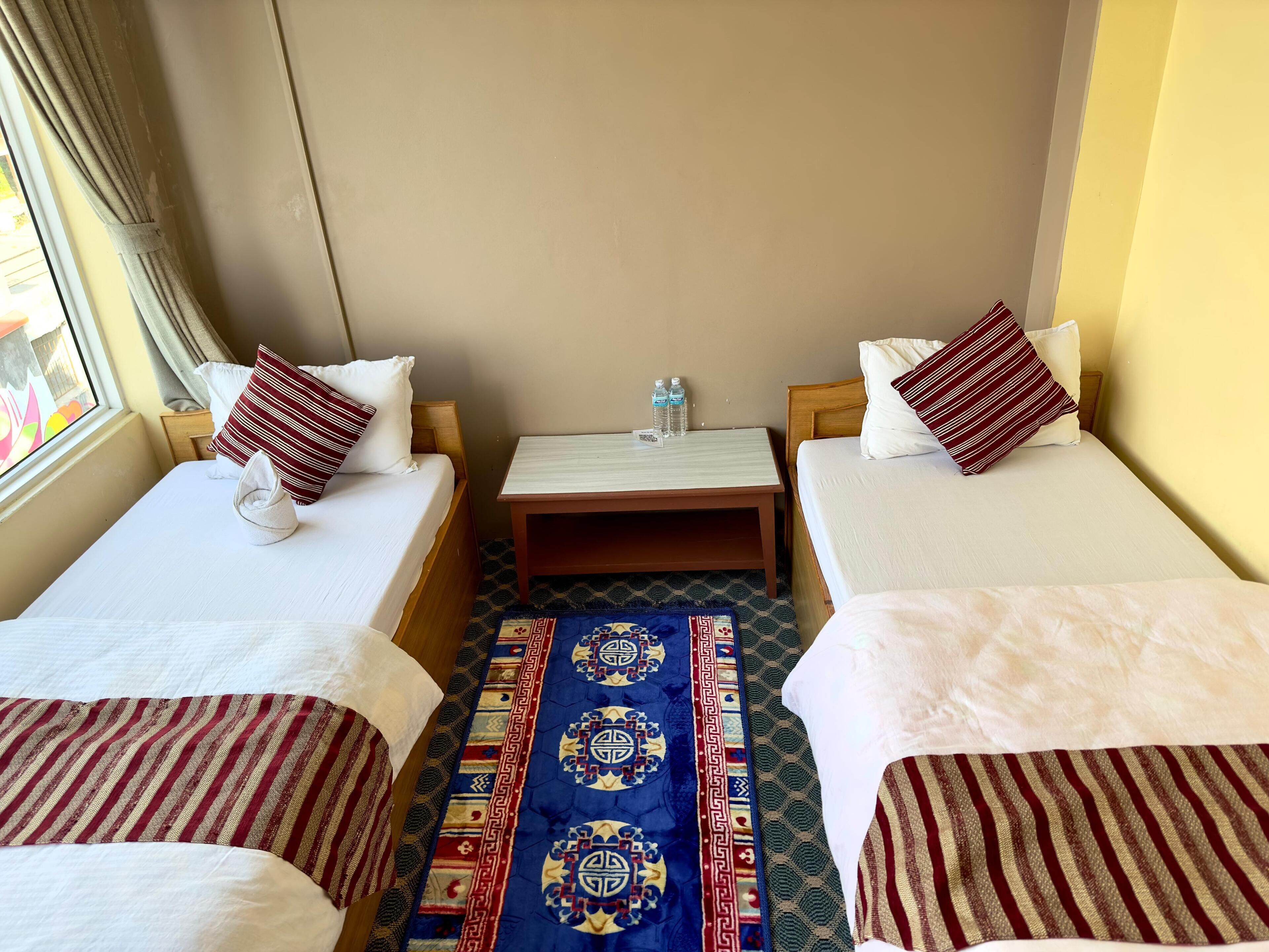 A hotel room with two single beds, a small table, and a patterned rug.