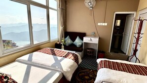 Ein Hotelzimmer mit zwei Betten, einem Nachttisch mit Ventilator, Blick auf Berge und einem durchgegangene Tür einsehbarer Badezimmer.