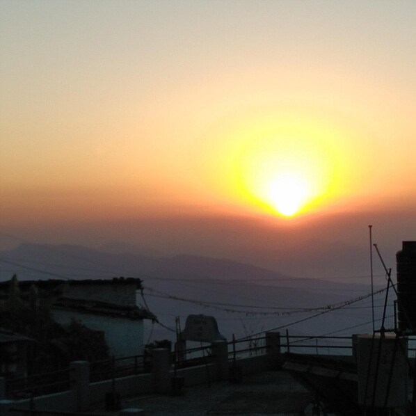 A sunset over a hilly landscape with a bridge and buildings in the foreground.
