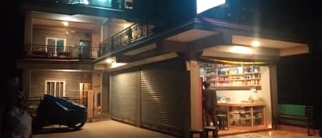 Un edificio de dos pisos con una persiana baja en la planta baja, un balcón en el piso superior y un coche estacionado adelante.