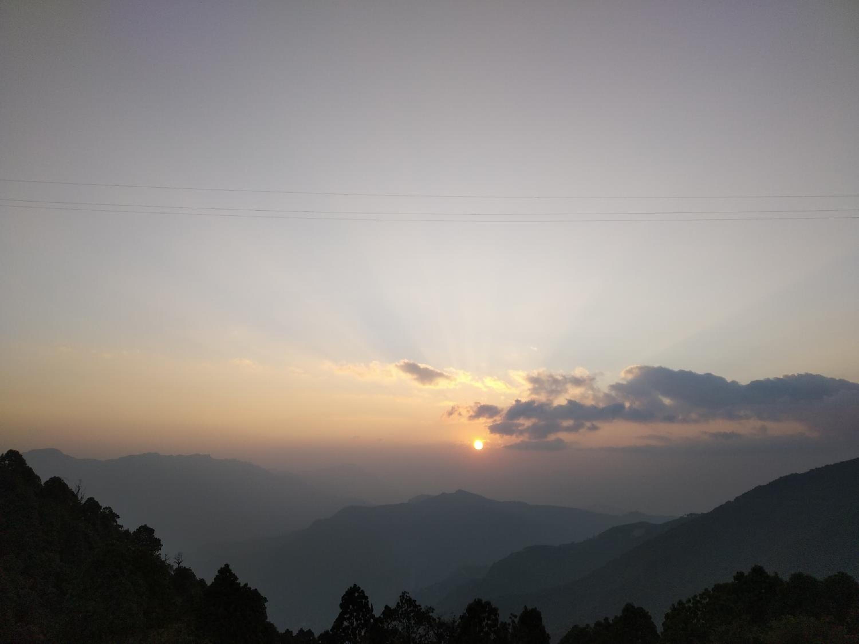 A mountainous landscape with a setting sun, power lines, and a clear sky.