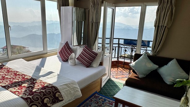 Ein Hotelzimmer mit Bett, einer Couch, einem kleinen Tisch und einem Balkon mit Bergblick.