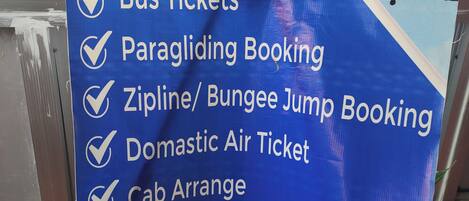 A sign listing services including bus tickets, paragliding booking, zipline/bungee jump booking, domestic air tickets, cab arrange, and hiking, sightseeing & trekking.