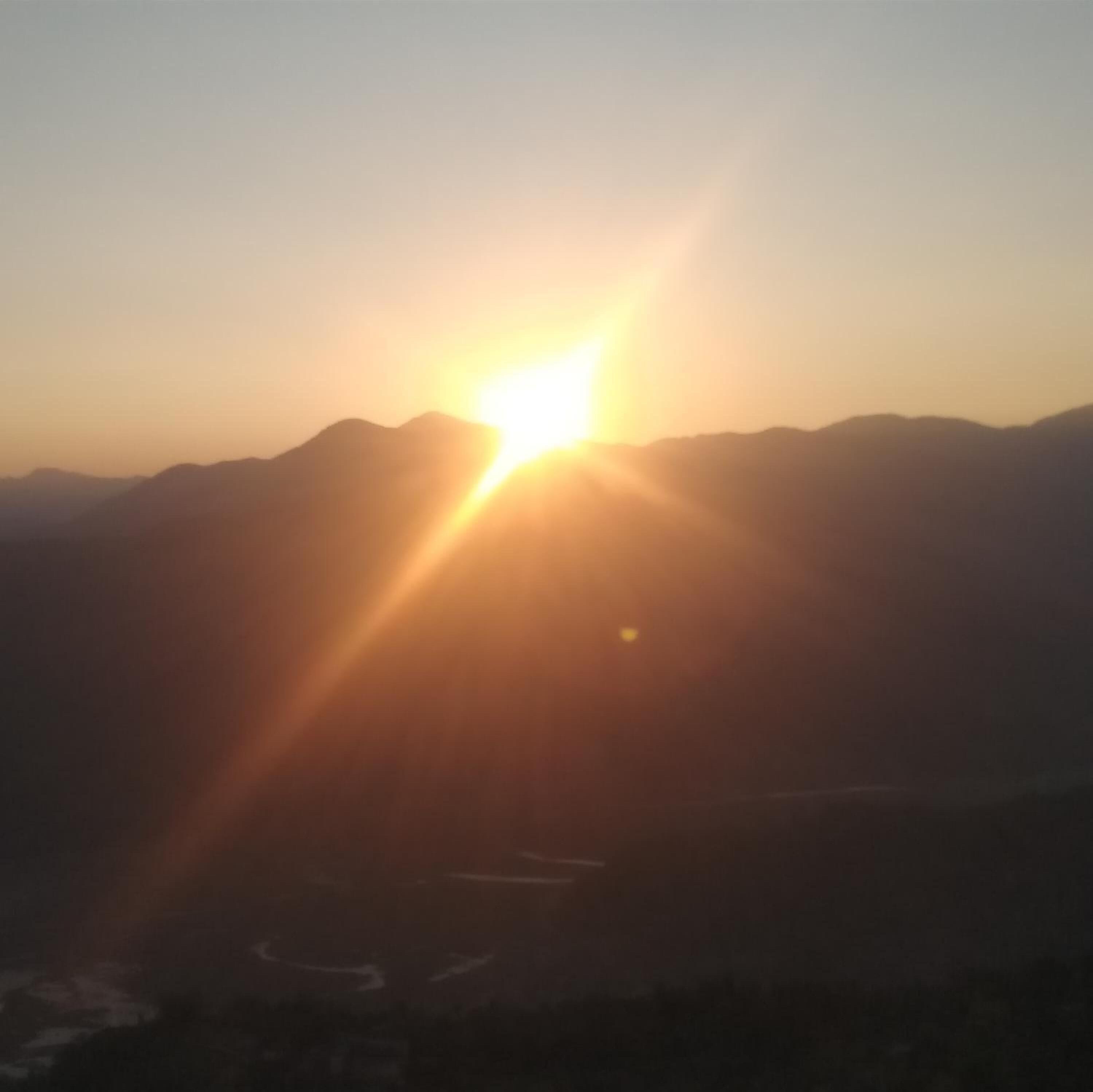 Un paisaje montañoso con el sol bajo en el horizonte, iluminando la escena con una luz brillante.