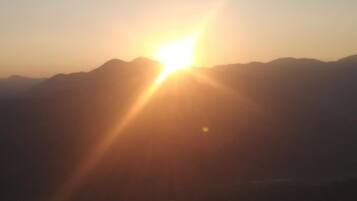 Un paisaje montañoso con el sol bajo en el horizonte, iluminando la escena con una luz brillante.