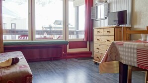 A cozy room with a bed, a wooden dresser, a table with a checkered tablecloth, and a TV on the wall. - Cosy apartment for 4 guests with WIFI, TV and balcony (Les Boisses)