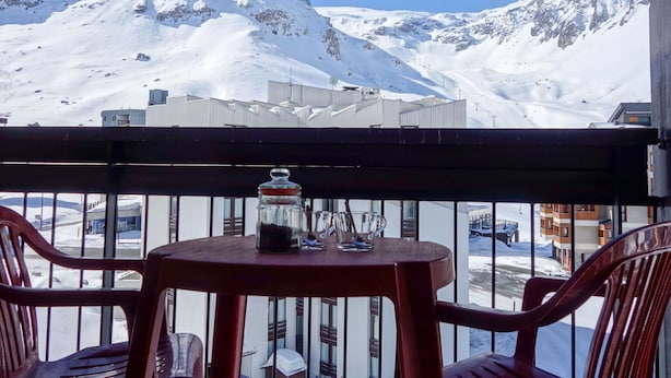 A balcony with a table and chairs, overlooking a snowy mountain landscape and buildings. - Cosy apartment for 4 guests with WIFI, TV and balcony (Les Boisses)