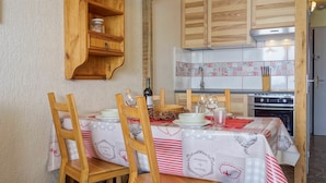 A dining area with a table set for four, wooden chairs, a hanging light fixture, and a kitchen with wooden cabinets and a tiled backsplash. - Cosy apartment for 4 guests with WIFI, TV and balcony (Les Boisses)