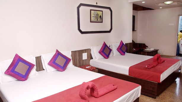 Two double beds with red and white linens, purple and brown patterned pillows, and red towels. - Viva Guest House (Panaji)