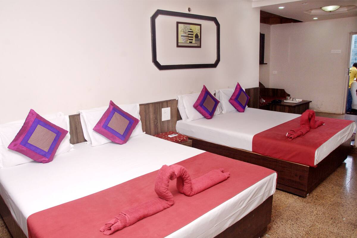 Two double beds with red and white linens, purple and brown patterned pillows, and red towels.