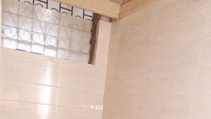 A bathroom with a toilet, a shower, and a blue bucket on the floor. - Viva Guest House (Panaji)