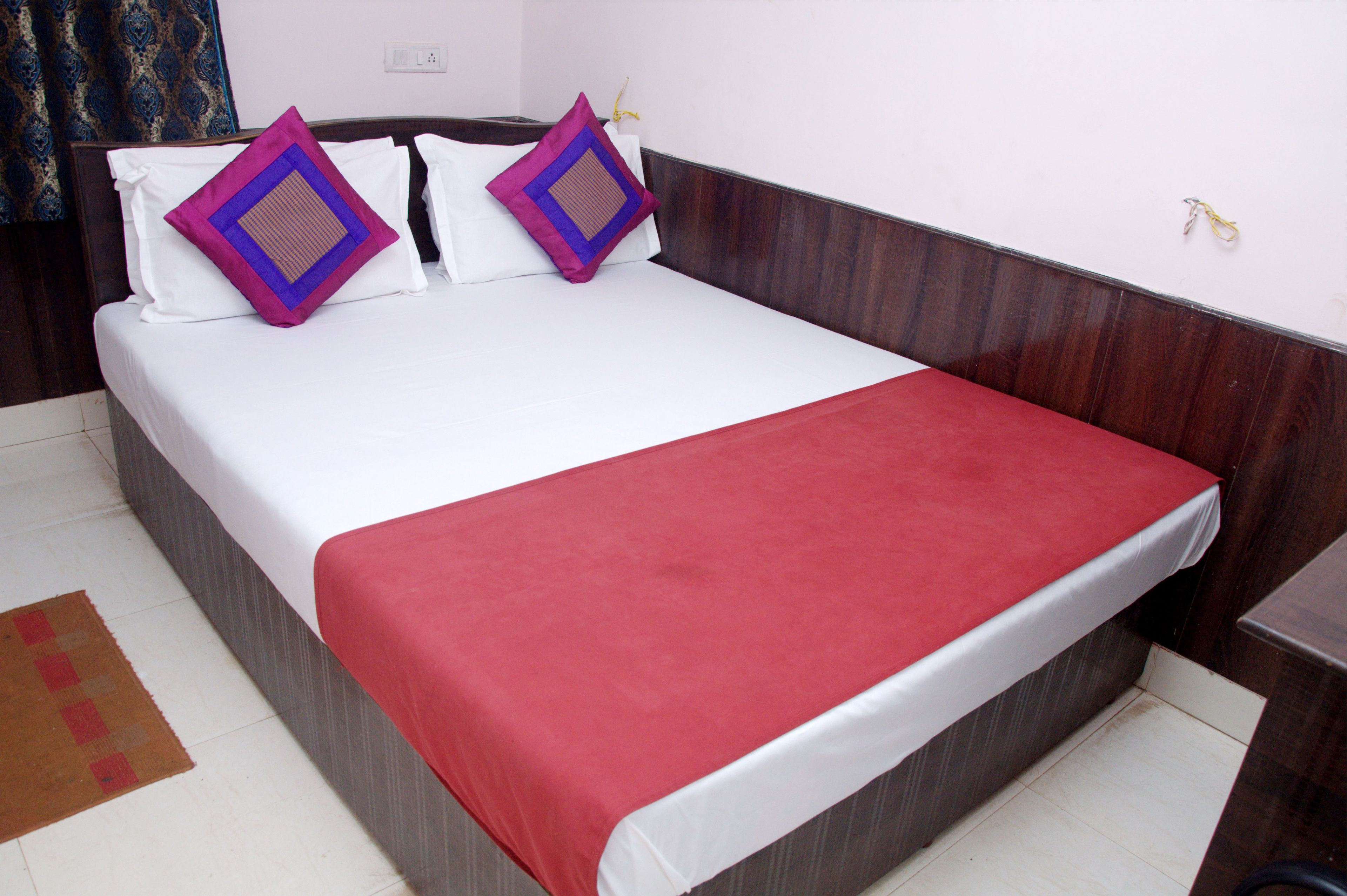 A neatly made bed with white and red bedding, two purple pillows, and a wooden headboard.