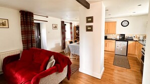Een gezellige woonkamer met een rode bank, een eethoek met een tafel en stoelen, en een keuken met houten kastjes en een koelkast.