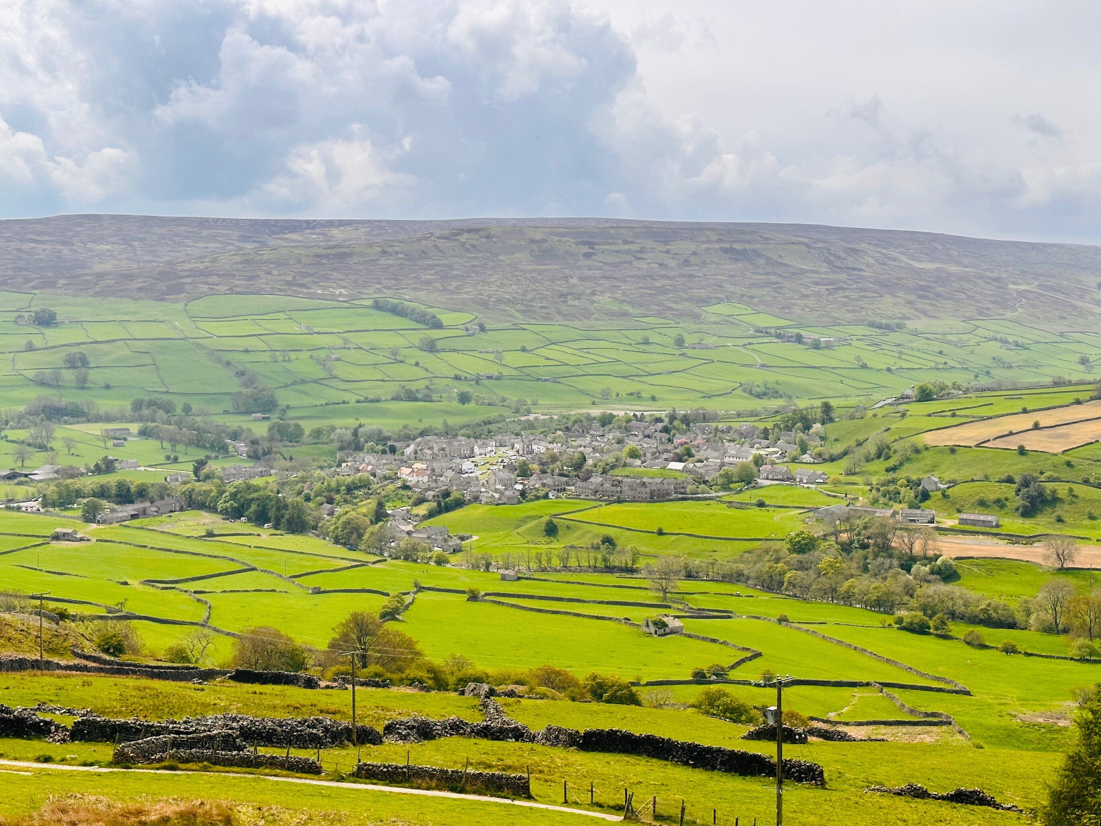 A rural landscape with a village, green fields, stone walls, and a cloudy sky.