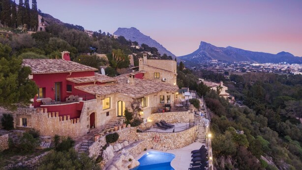 Une villa située sur une colline, dotée d’une piscine, de murs en pierre et offrant une vue sur le paysage environnant.
