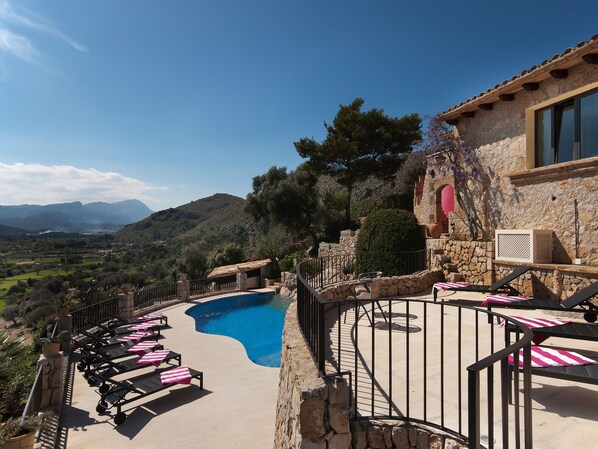 A pool area with lounge chairs and a stone building with a view of the mountains. - SundanceMallorca, Port de Pollensa’s Finest Luxury Residence, Stunning Sea Views (Pollença)
