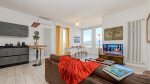 Ein modernes Wohnzimmer mit einer Couch, einem Couchtisch, einem Fernseher und einem Essbereich mit Tisch und Stühlen.