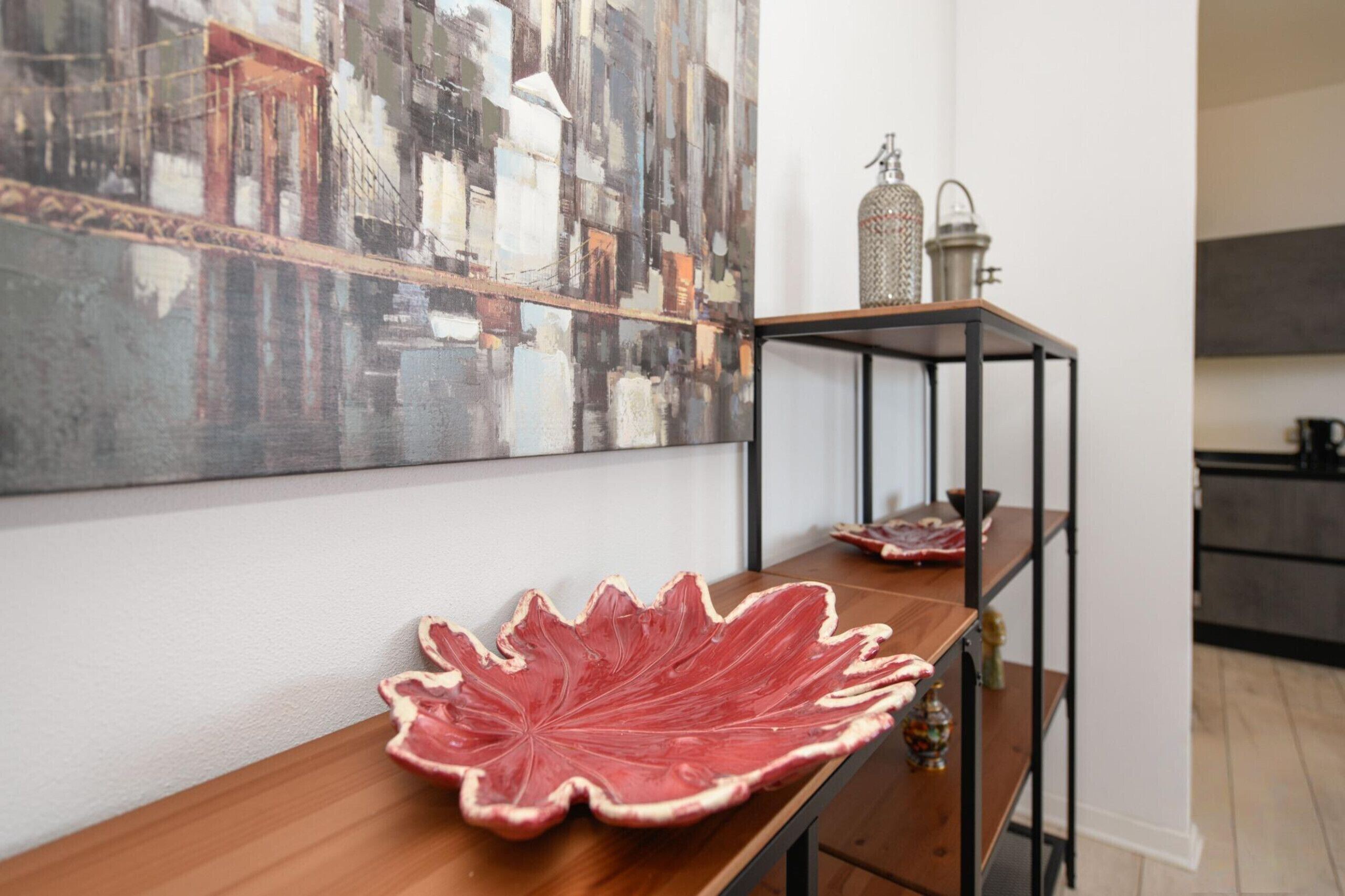 A modern kitchen with a wooden table, a metal shelf unit, and a cityscape painting on the wall.