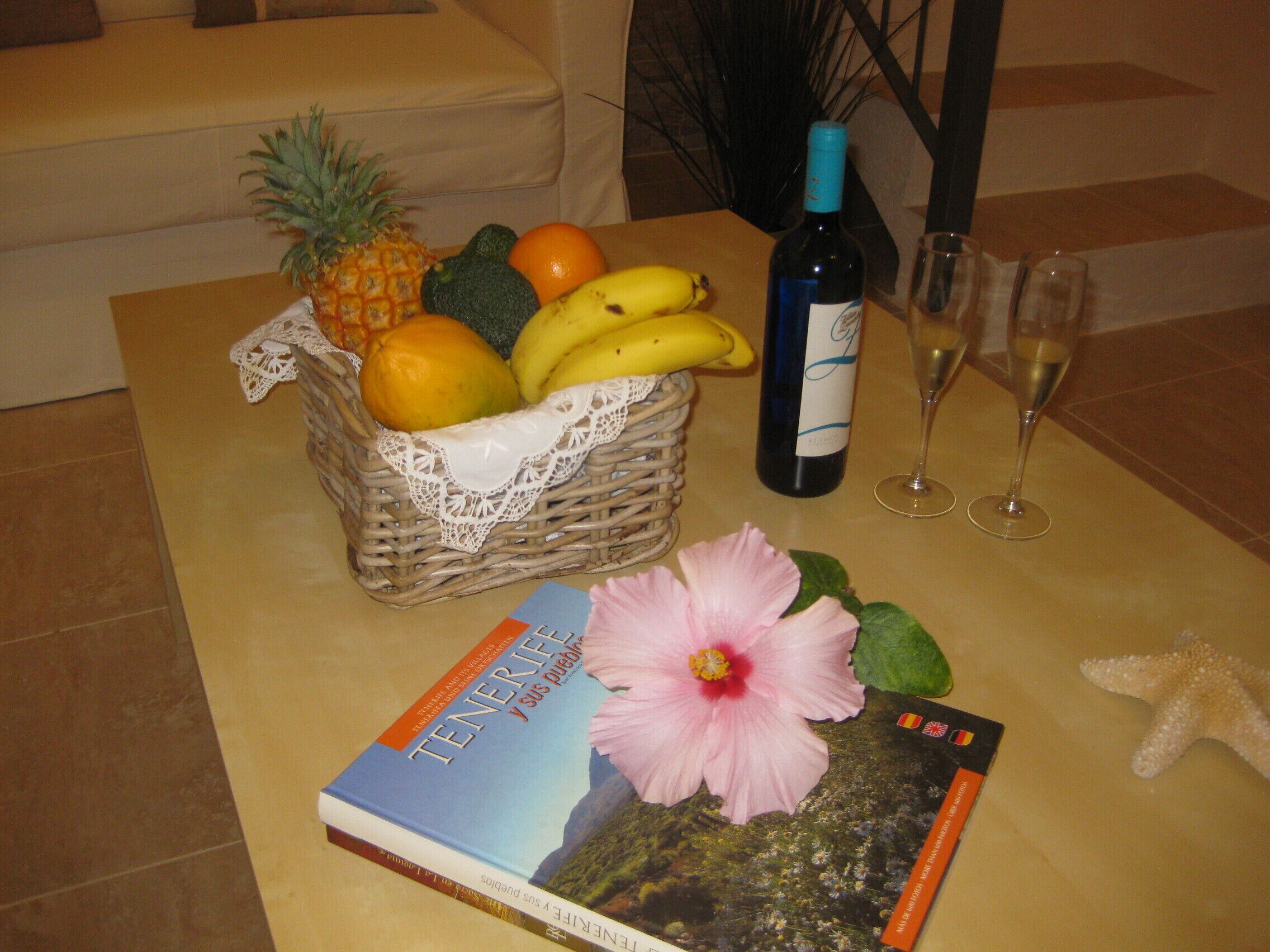 Ein Tisch mit Obstkorb, einer Weinflasche, zwei Gläsern, einem Buch, einer Blume und einem Seestern.