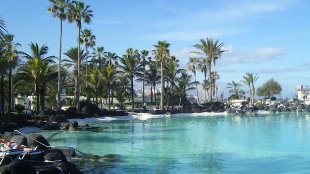Een zwembad van een resort, omringd door palmbomen en rotsen.