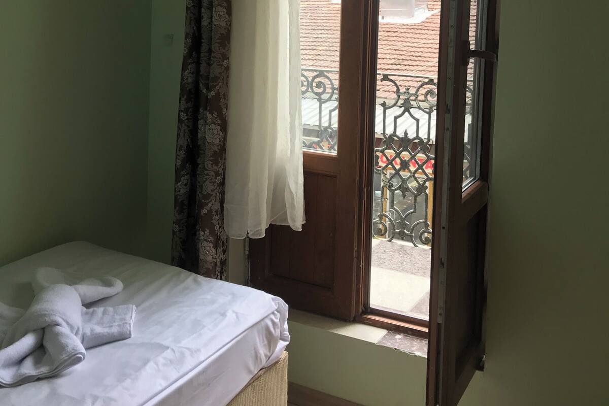 A room with a bed, a window with a curtain, and a view of the outside balcony.