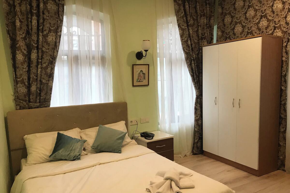 A bedroom with a bed, nightstand, lamp, wardrobe, and curtains.
