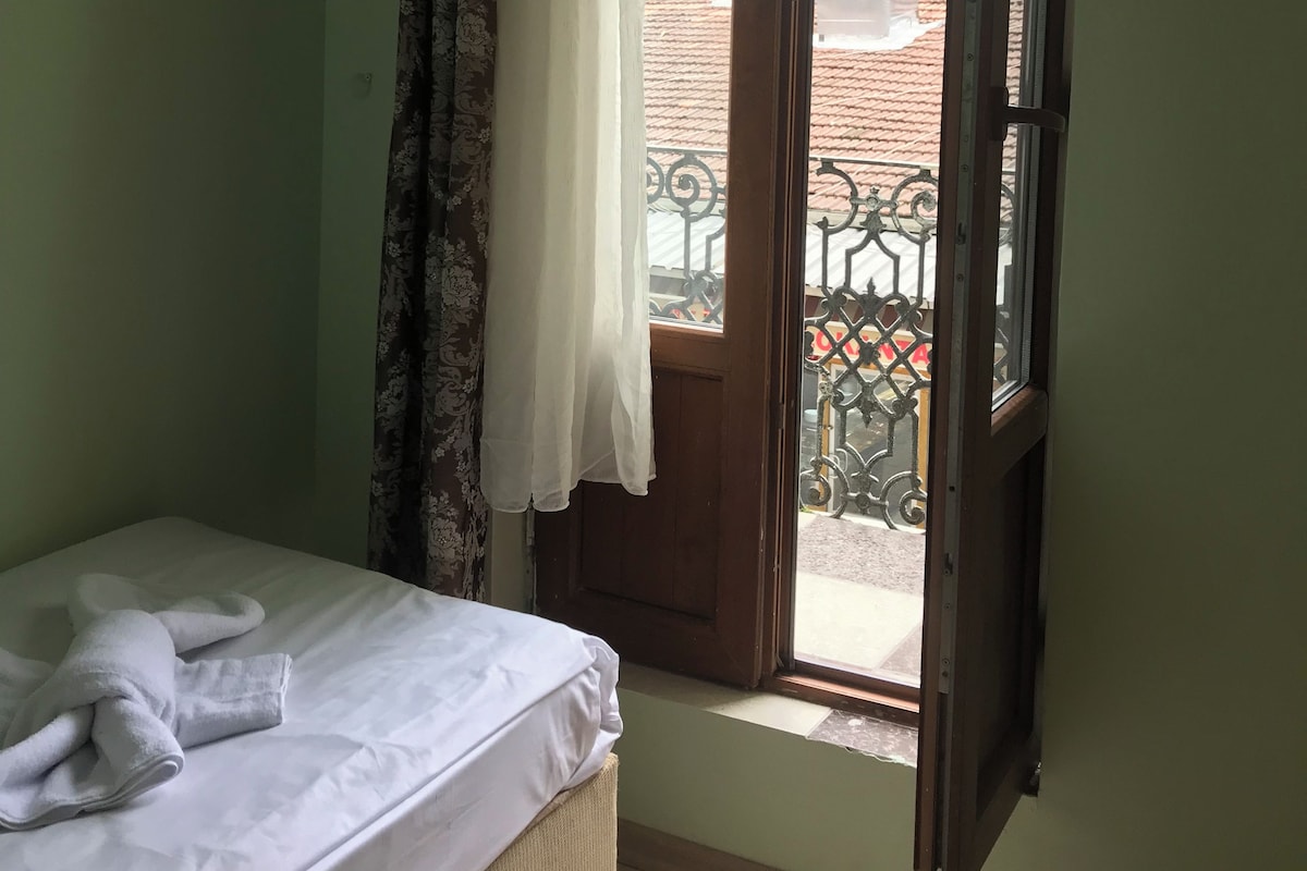 A room with a bed, a window with a curtain, and a view of the outside balcony.