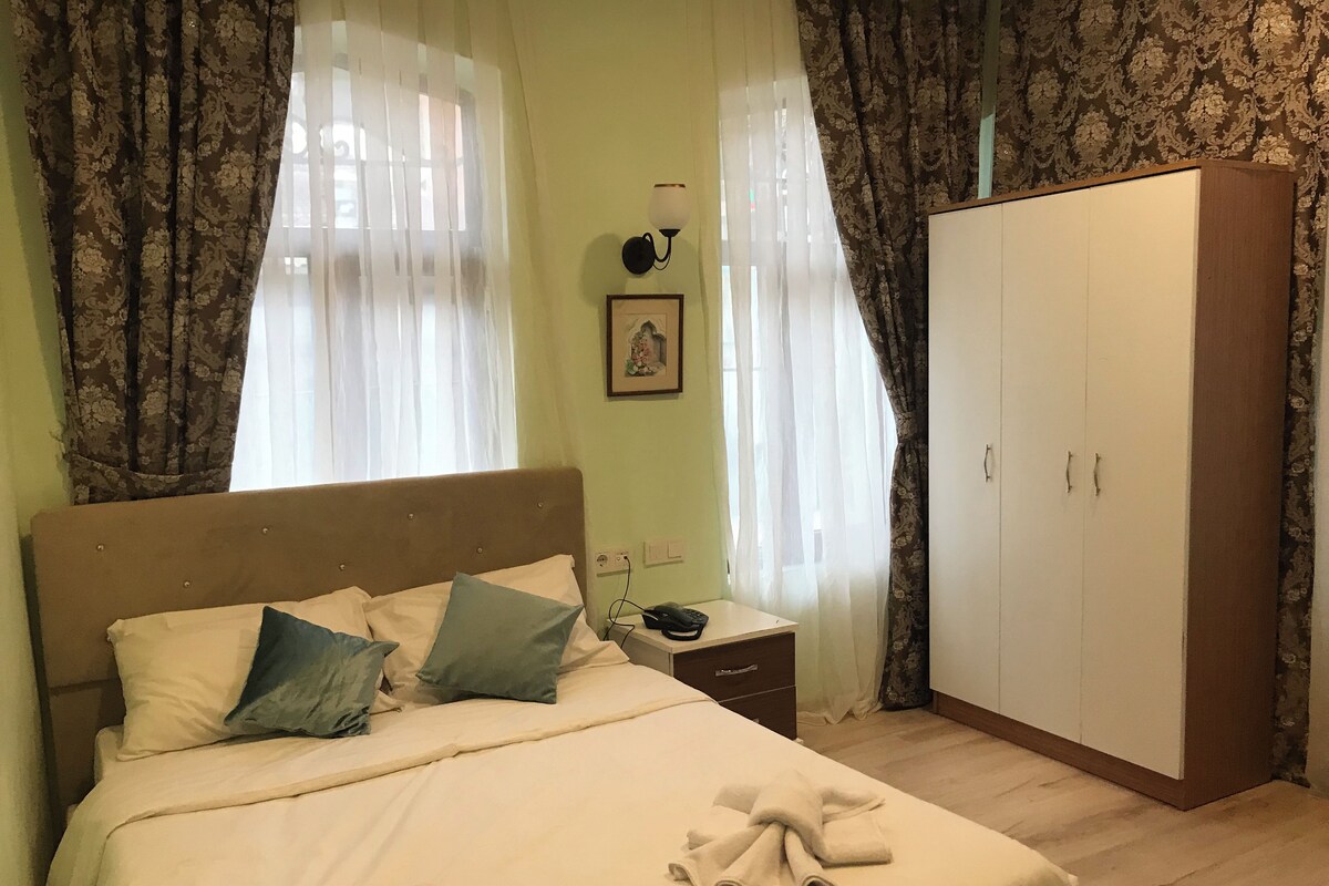 A bedroom with a bed, nightstand, lamp, wardrobe, and curtains.