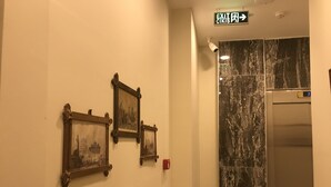 A hallway with three framed pictures on the wall, an exit sign, and a marble elevator. - Historial Hotel (Istanbul)