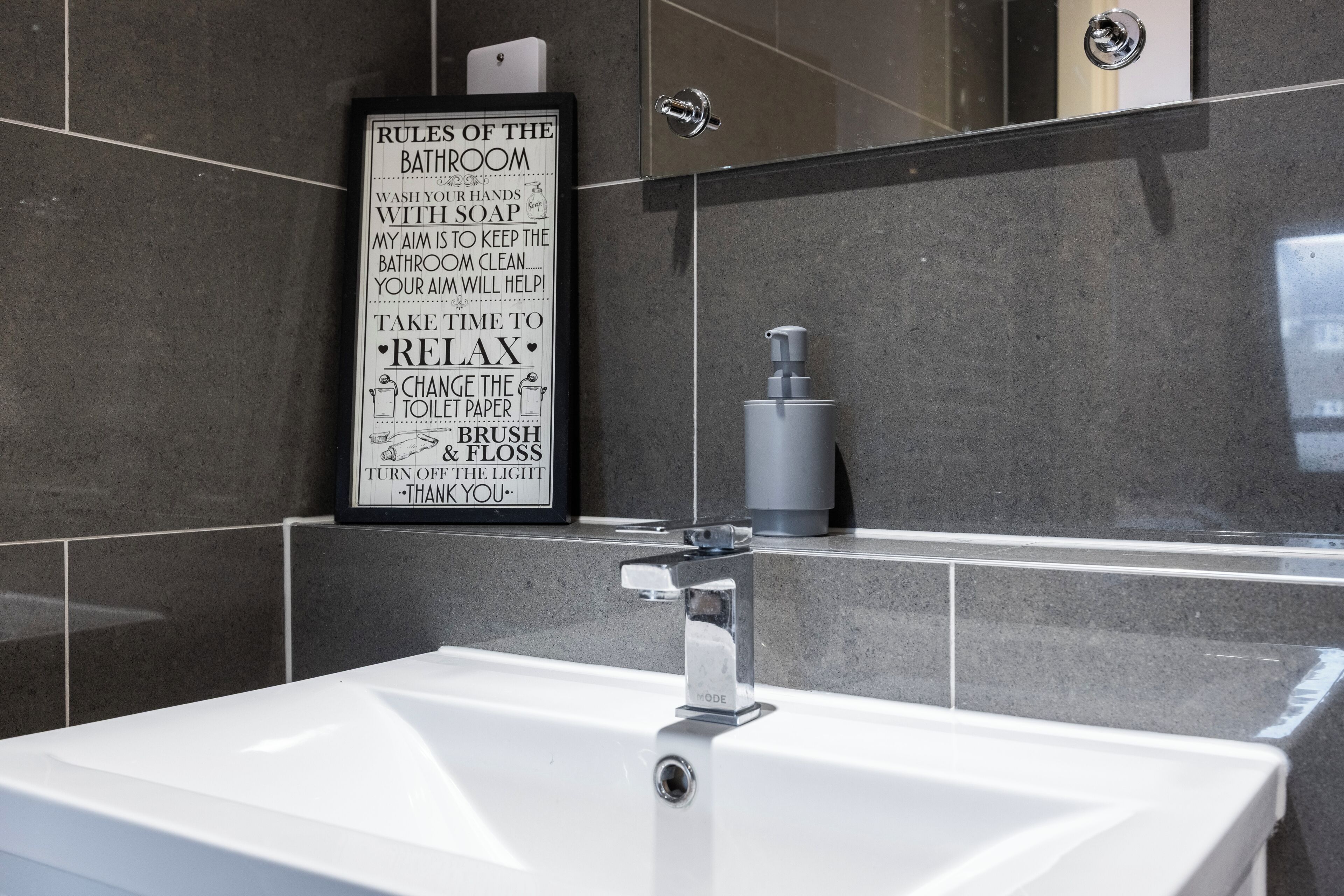 Ein modernes Badezimmer mit einem weißen Waschbecken, einem Spiegel und einem Schild mit Badezimmerregeln.
